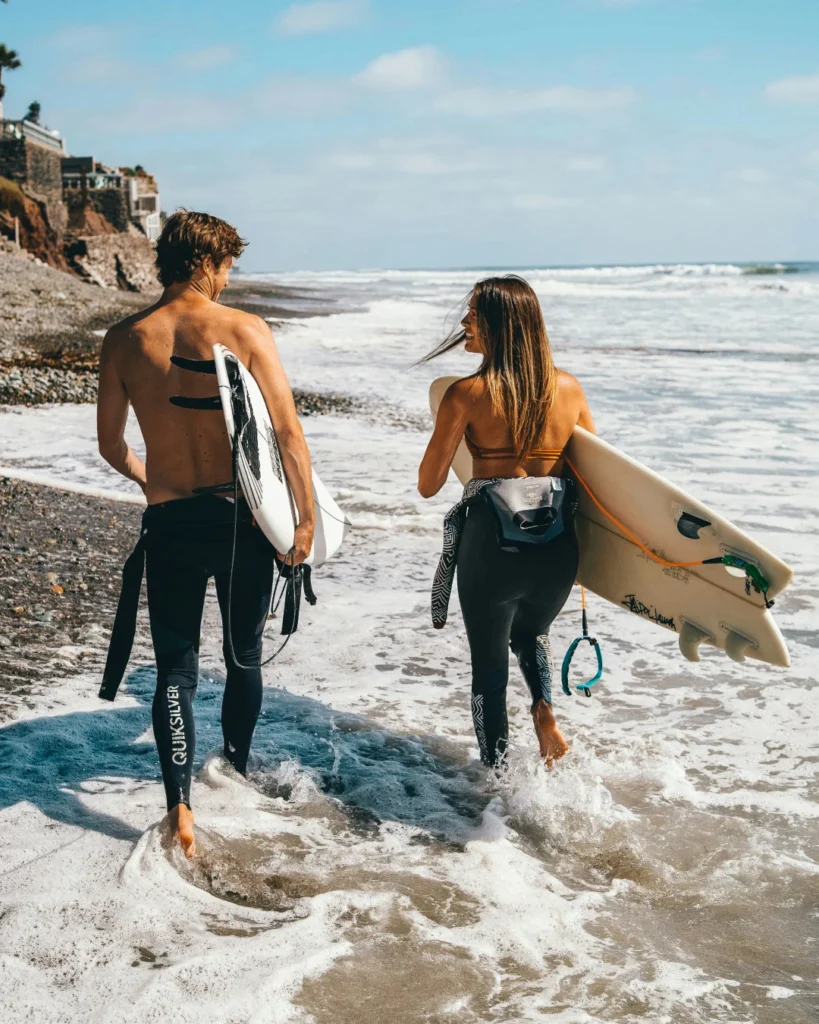 A couple holding surfboards and talking at the shoreline